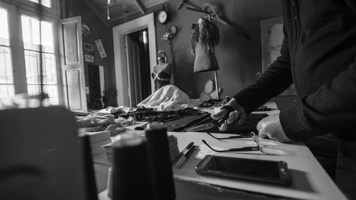A black and white image capturing a seamstress working in a vintage workshop with tools.